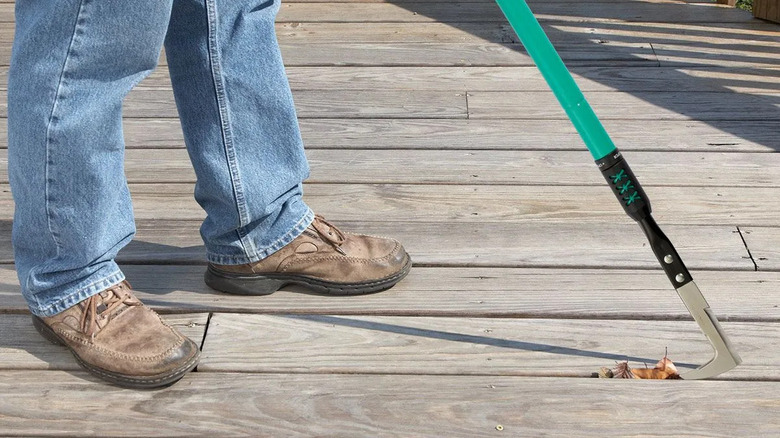 Close-up of a person scraping the gaps between deck boards with a crevice cleaning tool