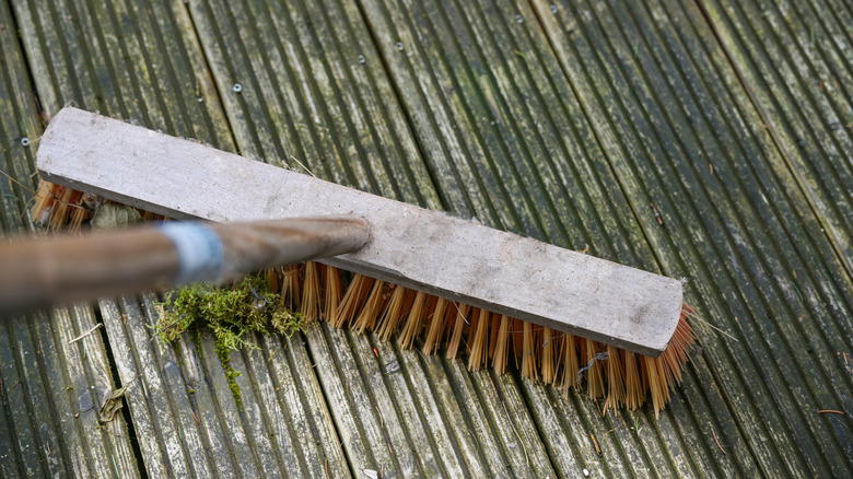Close-up of a stiff broom removing debris from a wooden deck