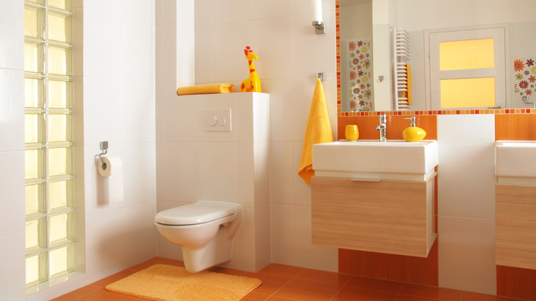 A white and orange bathroom with orange elements including towels, containers, and rugs