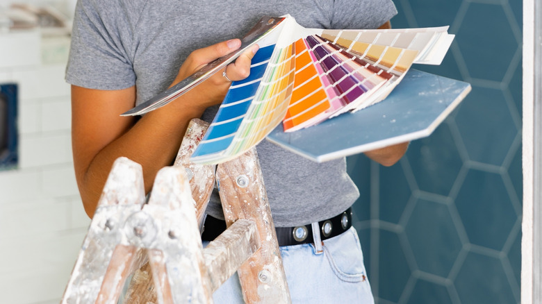 A person leaning against a painted ladder with color samples with blue and white tile in the background