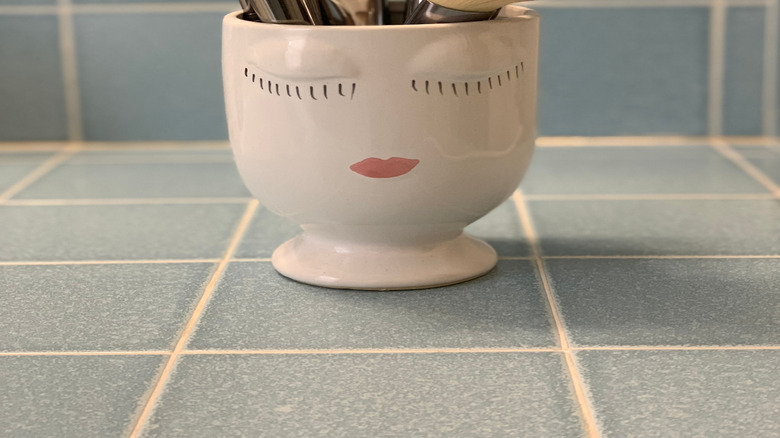 Vintage planter holding makeup brushes in a tiled bathroom