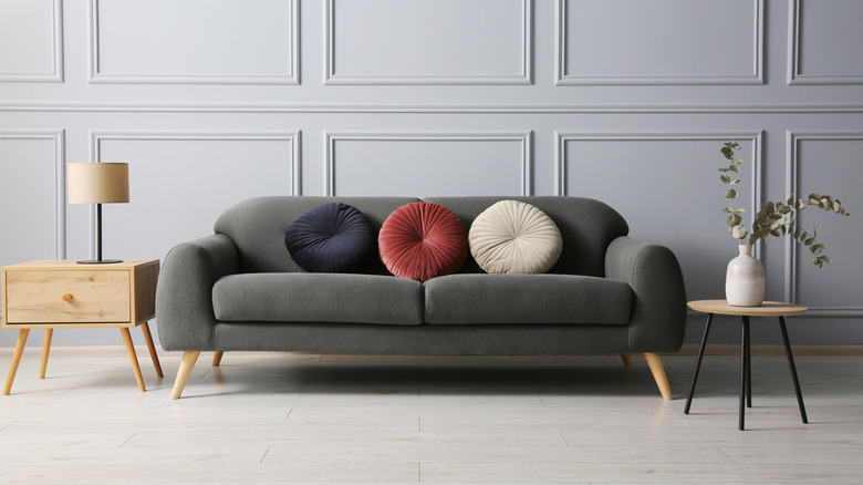 A minimalistic living space with a plush green sofa and two end tables with only single items on them