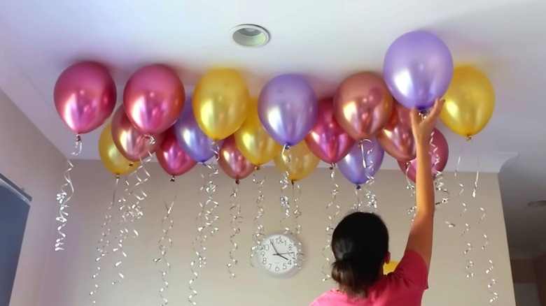 woman sticking shiny, colorful balloons to ceiling with hidden adhesive