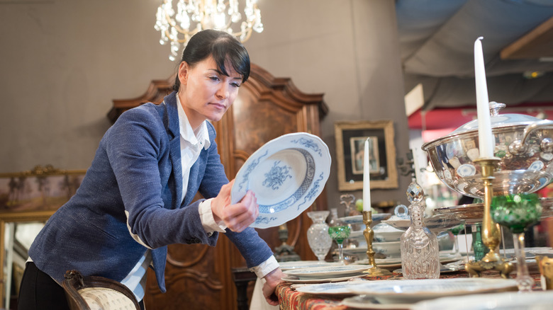 A woman looks at the bottom of a porcelain plate in an antique store.