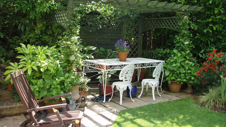 A nice, relaxing shady corner of a garden with tables, chairs, and a variety of different plants