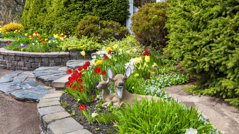 Two laying down deer statues in the middle of a gorgeous flower garden
