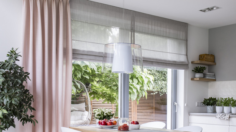 Kitchen sliding windows with layered window treatments featuring gray Roman shades and pink curtains