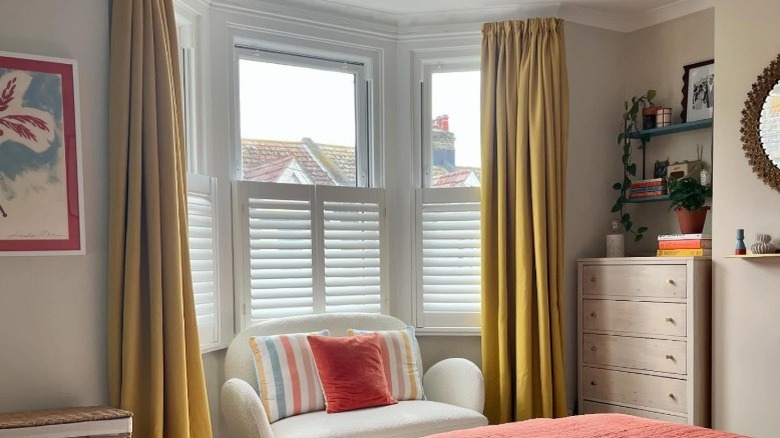 Bay window with white half shutters and dark yellow drapes