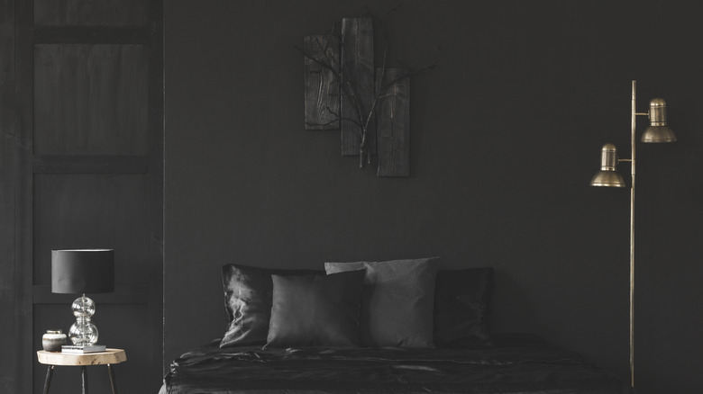 An all black bedroom with a gold lamp to the side.