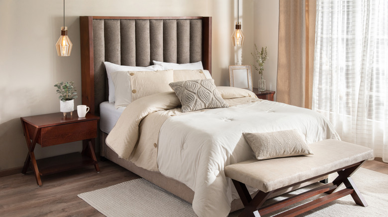 A neutral colored bedroom with a nightstand and bench.