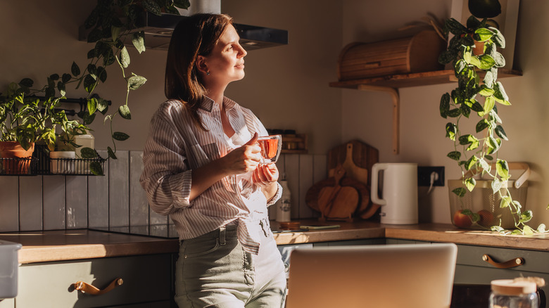 A smiling woman looks towards a window while standing in her kitchen.