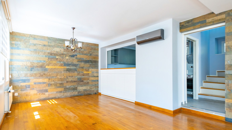 An empty dining room has a wood-covered accent wall and a pass-though window into the kitchen.