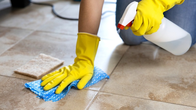 person in yellow rubber gloves spraying and wiping white vinegar on tile floor