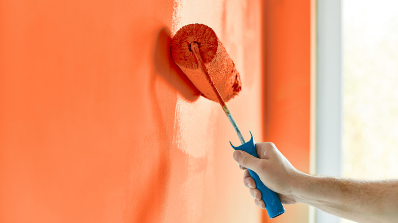A male hand using a roller to paint a wall orange