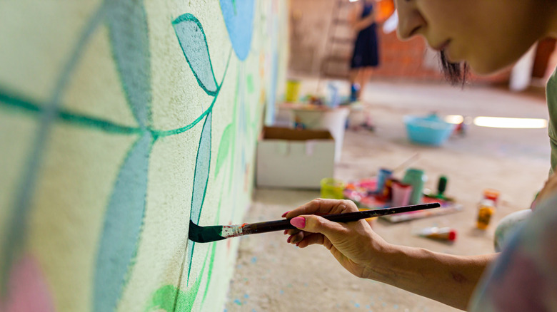 A woman hand painting a wall mural on an interior wall