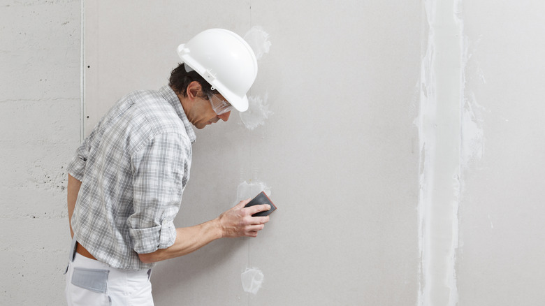 Man sanding mud on drywall sheets