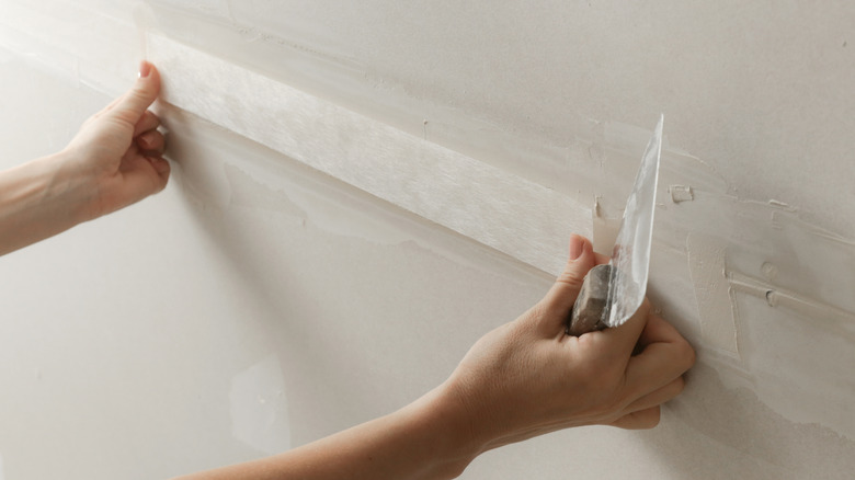 Person adding tape to the seams between two sheets of drywall