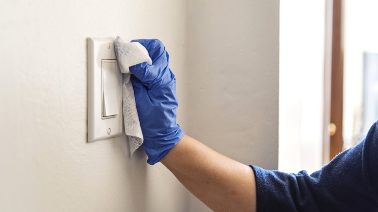 Person cleaning kitchen light switch with cleaning wipe