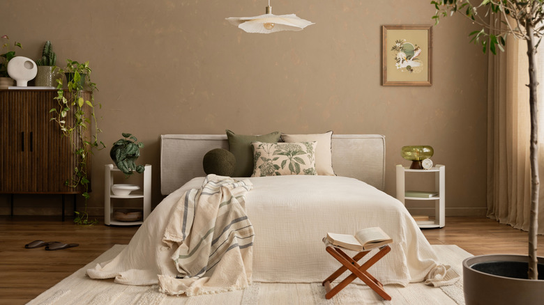 A bed with cream bedding, modern furniture, plants and brown walls