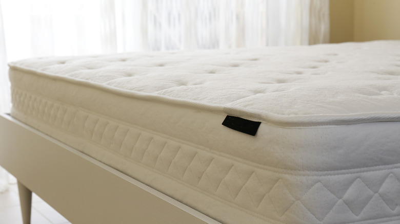 White bare mattress on a smart white bed frame with sheer curtains in the background