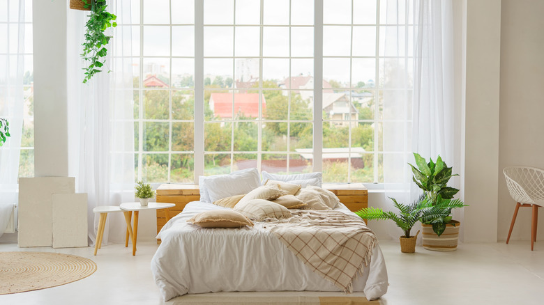 Floor to ceiling bedroom windows with white panels with a double bed sitting in front of them and made up with white bedding.