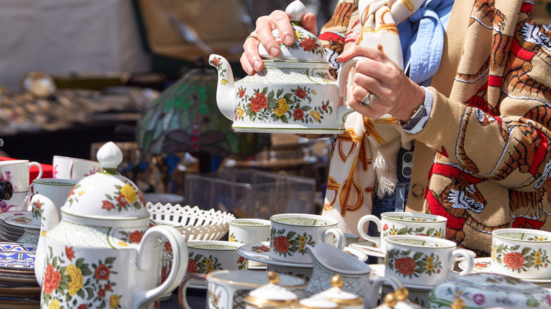 Person holding patterned teapot with red and yellow roses