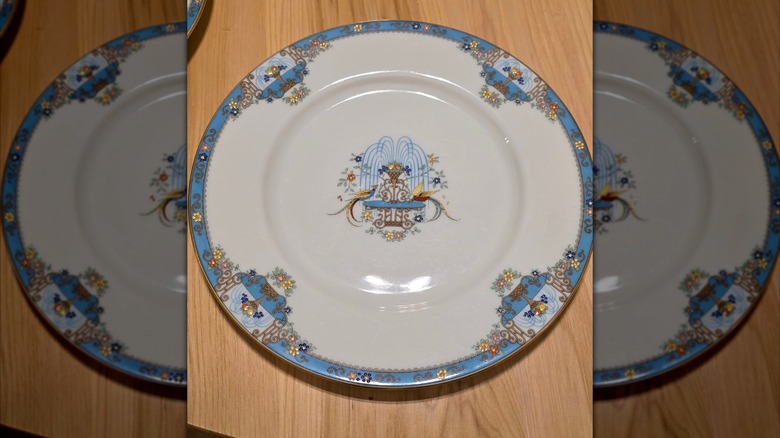 Cup and saucer set of Lenox Fountain pattern, which features gold edge with fountain and two birds, on a table