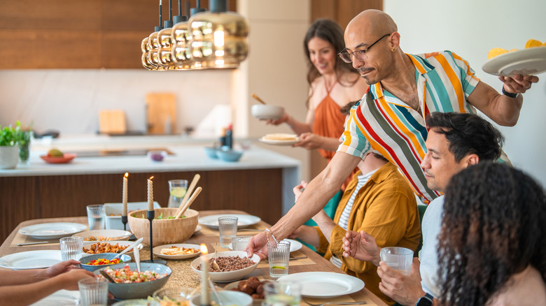 A dinner table with people waiting to eat as plates are set down.