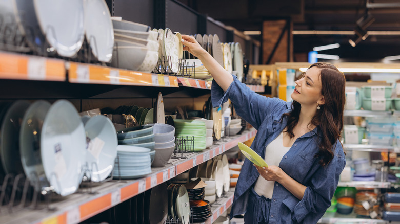 A woman in a denim shirt shopping for dishes on shelves at a store