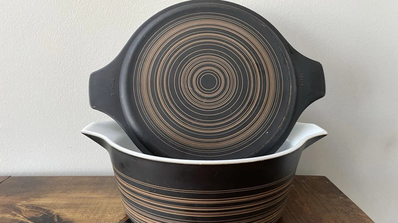 A Pyrex covered casserole dish in the brown and orange Terra pattern, featuring a dark brown background with lighter brown-orange stripes