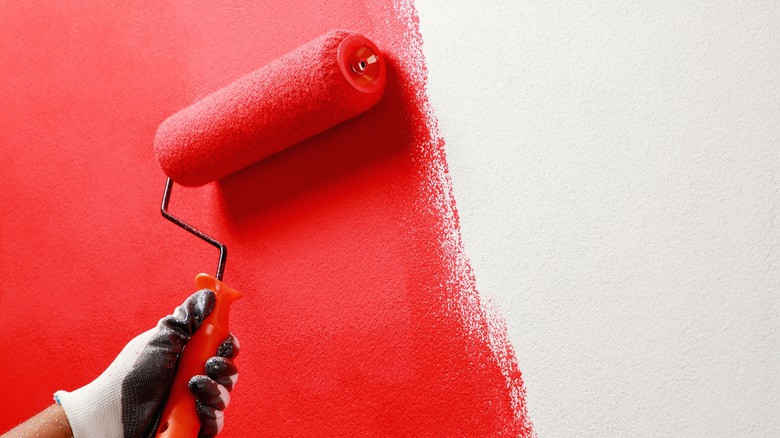 A red paint roller runs up and down a blank, white wall, leaving half of the image coated red.