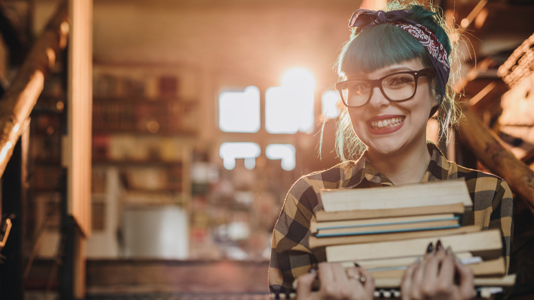 A smiling person holds a stack of books in a book store
