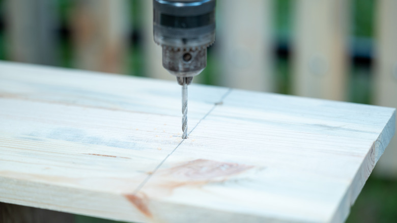 Screwdriver driving nail into wooden fence board