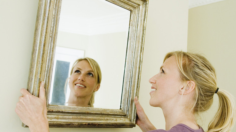 Woman lifting mirror off wall 