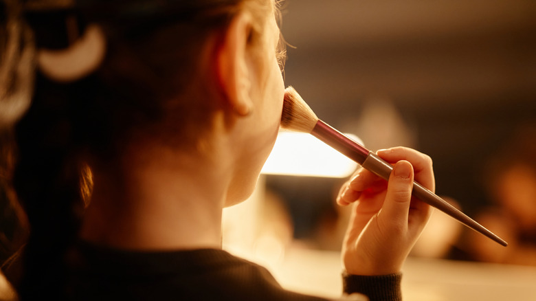 Someone applying blush at a vanity