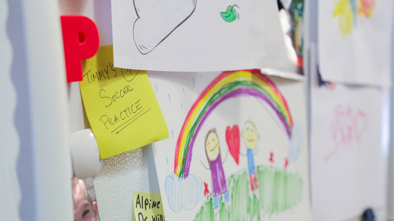 Refrigerator door cluttered with kids' art and other items