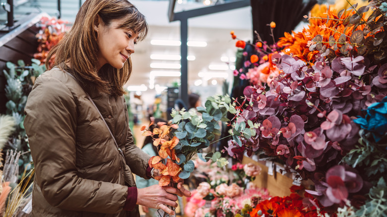 A woman holds a bunch of faux flowers in a retail store.