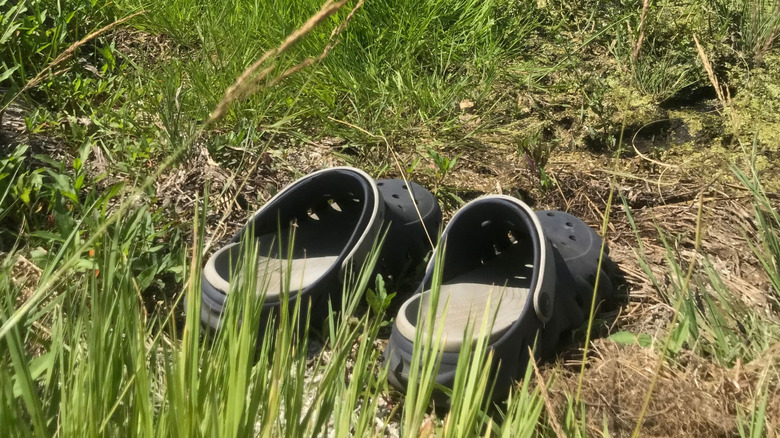 Two black and gray Crocs on the ground partially covered by grass