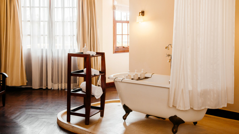 white shower curtain in bathroom around freestanding claw foot tub next to large window