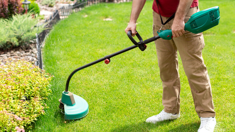 A man using a weed wacker to trim long grass at the edge of a lawn