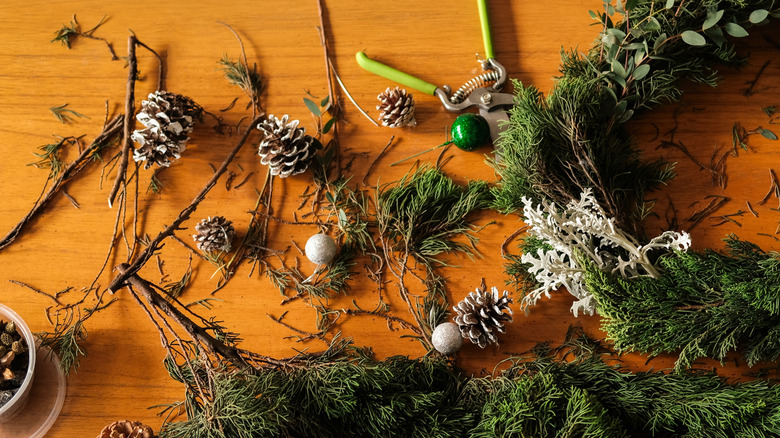 A person adds pinecones to a wreath made of real spruce tree foliage.