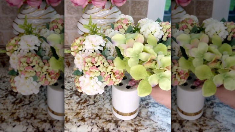 A person fills a toothbrush holder with artificial flowers.
