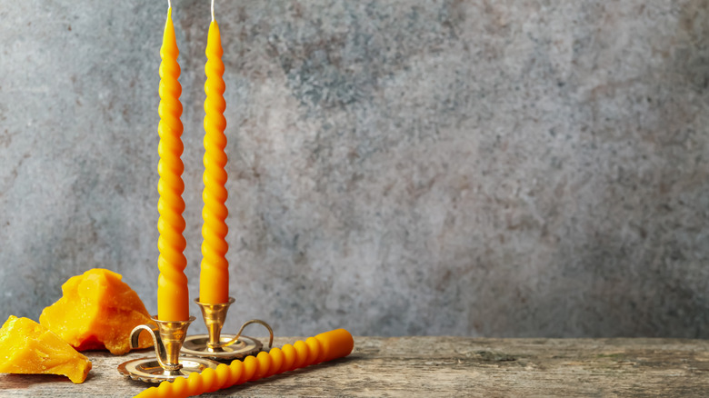 Twisted taper candles in brass candle holders sitting on a table with wax.