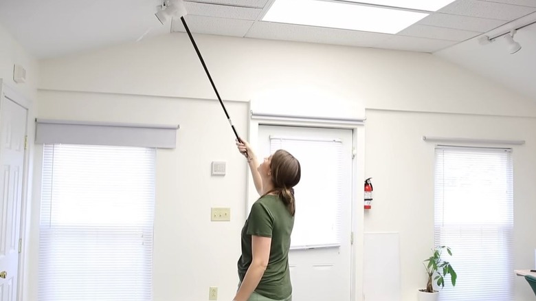 A person cleaning the ceiling with Dollar Tree broom handle and cloth