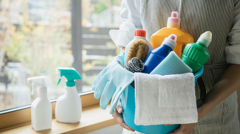 A person holding a bucket full of cleaning products