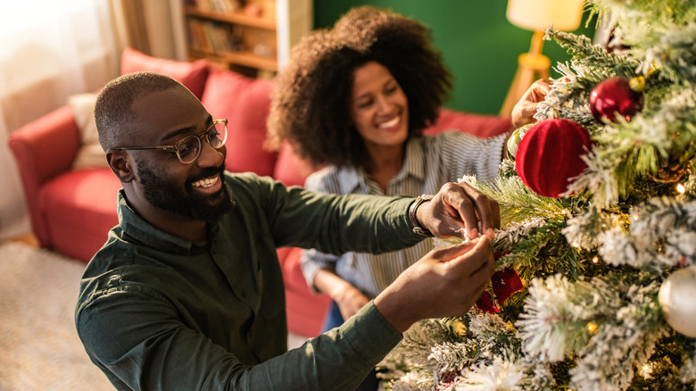 A smiling couple decorate a Christmas tree
