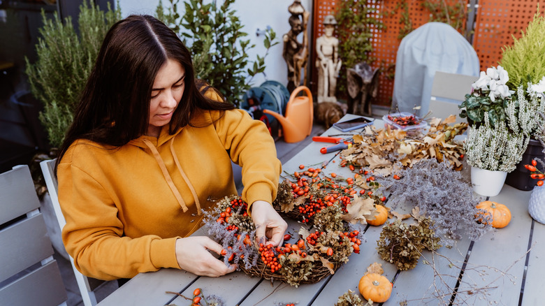 Woman crafting autumn wreath with pumpkins and leaves