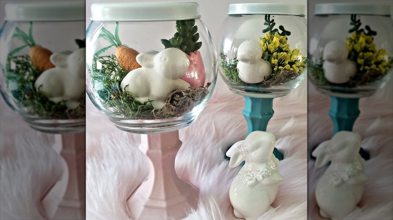 Glass fish bowl vase with white decorative bunny, grass, carrot and easter egg inside next to a bowl with a white duck, and then sat on a pink fluffy covering