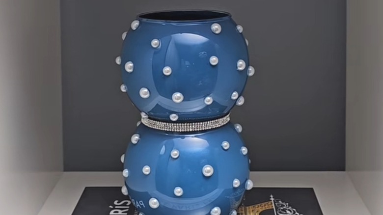 Dark blue bubble vase studded with faux pearls sits on a book about Paris in a shelf