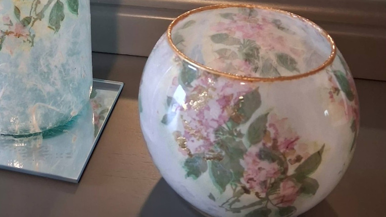 Flower decoupaged fish bowl vase with gold glittering rim next to a bottle decorated the same way